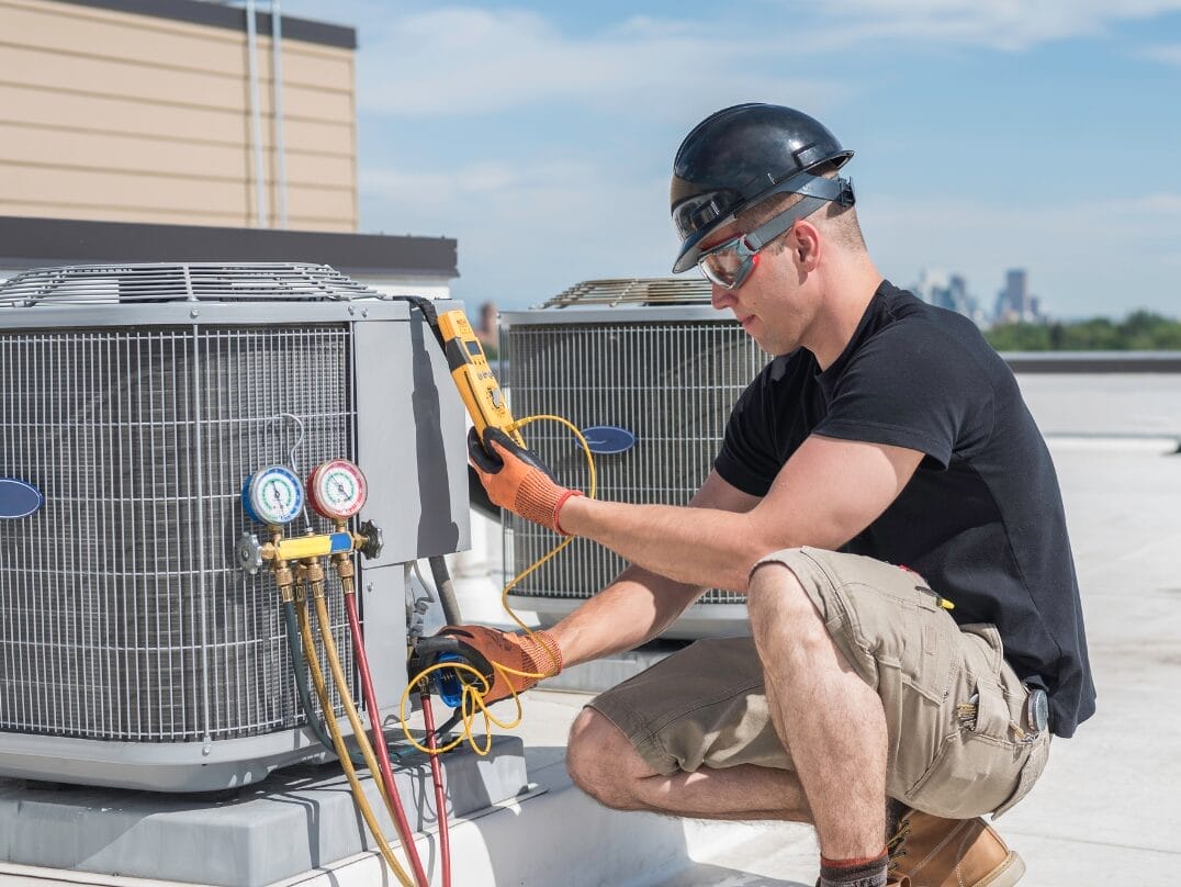 A technician inspecting a commercial HVAC system on a rooftop with a cityscape in the background.
