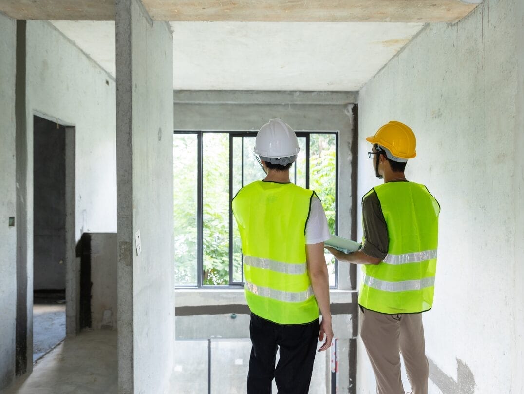 Two inspectors in safety vests and hard hats evaluating a commercial building under construction.